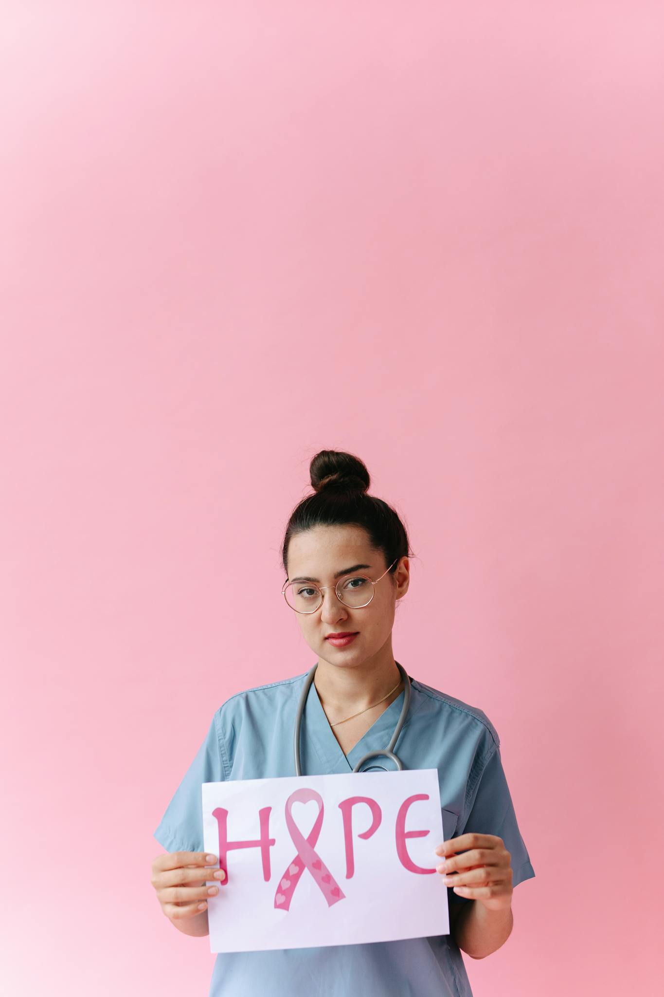 Medical professional promoting breast cancer awareness with a hope sign on a pink background.